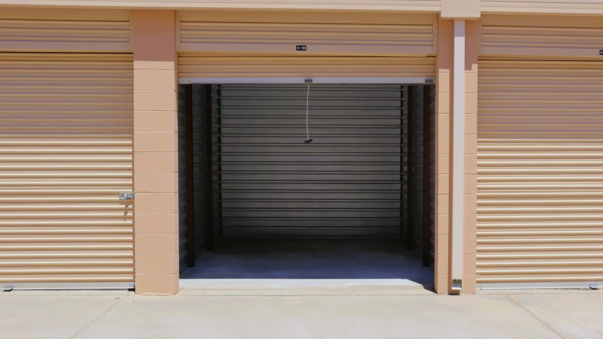 An empty drive-up unit at Sierra College Self Storage with its roll-up door open between two closed tan doors